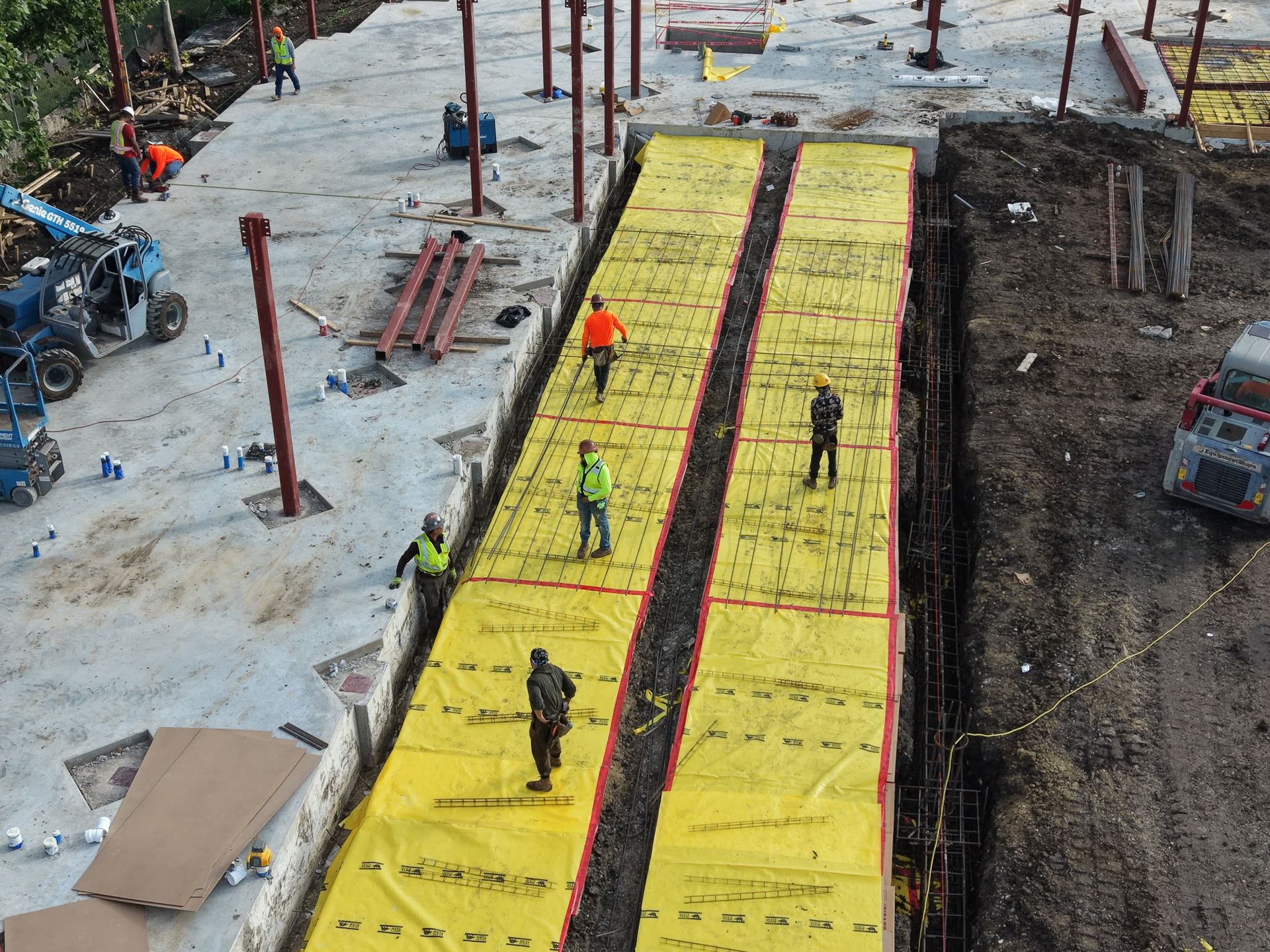 Construction workers walking on two bright yellow temporary walkways beside a muddy site