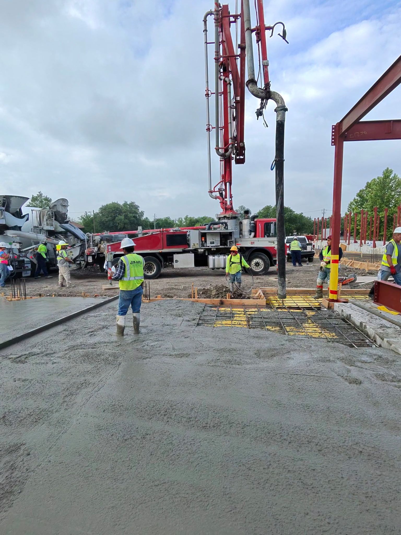 Construction crew pouring concrete around a red pump truck on a wet job site