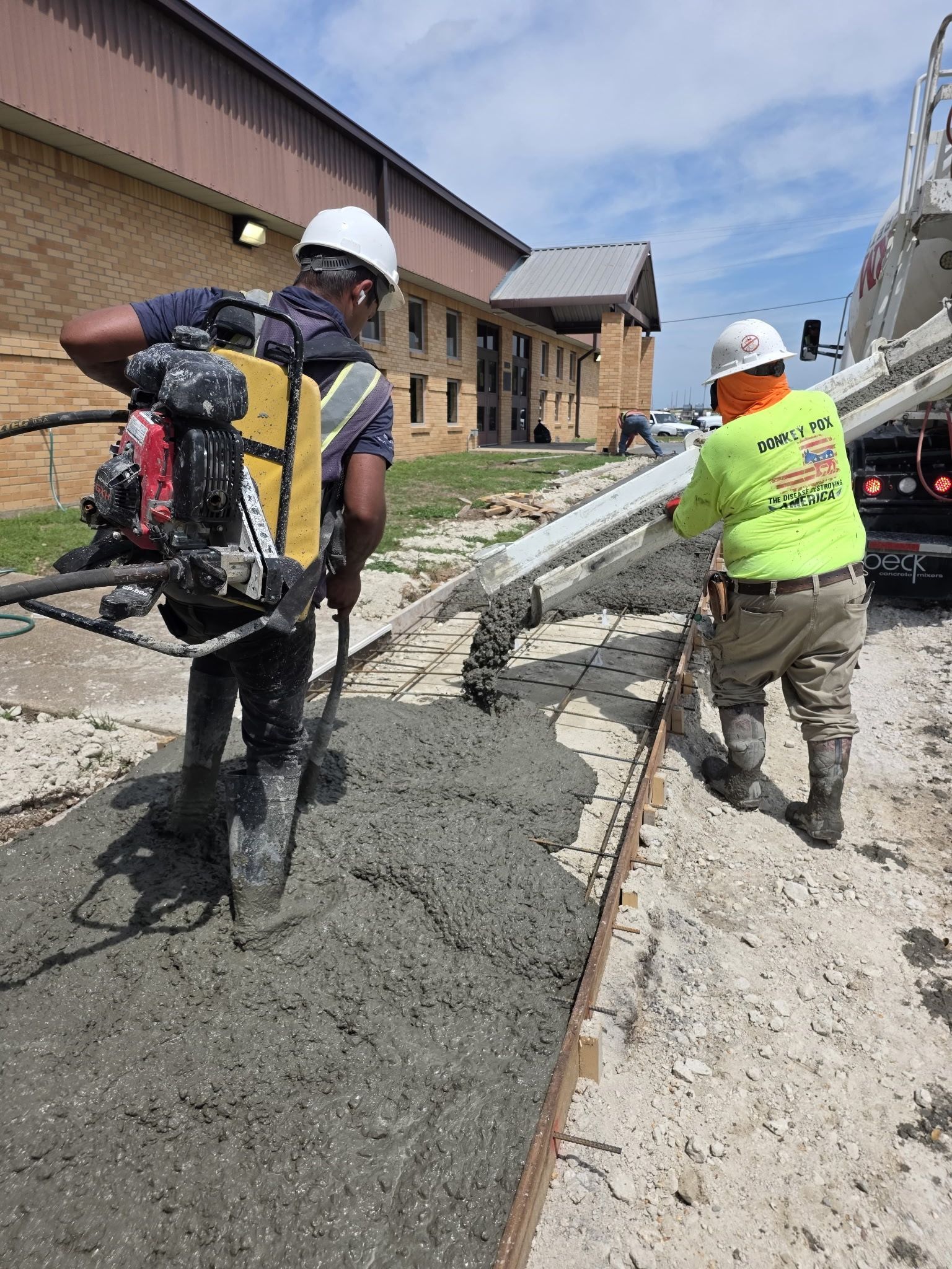 Construction workers using a machine to pour concrete beside a building under repair
