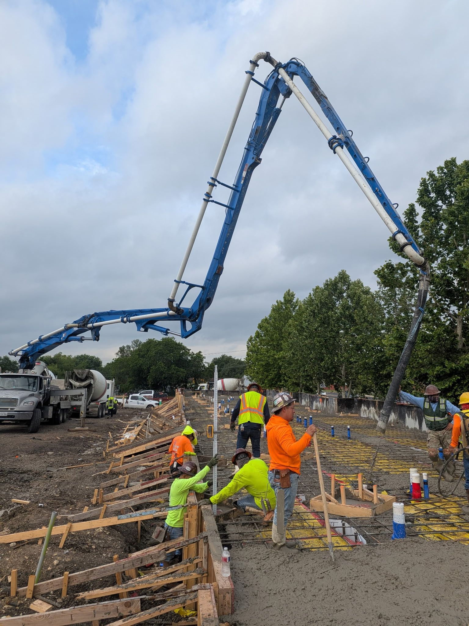 Construction crew pouring concrete with a long boom pump at a roadwork site