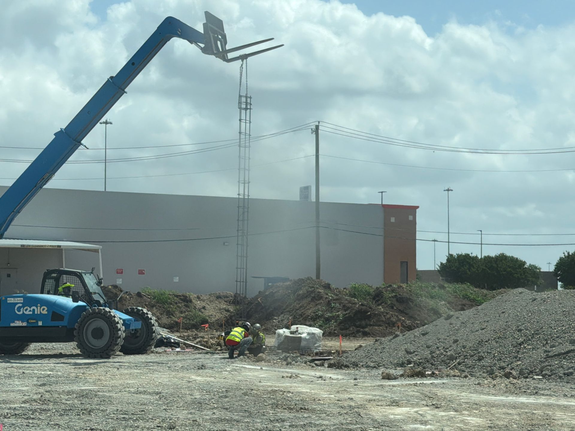 Construction site with a crane lifting a metal frame beside a tractor and gravel pile