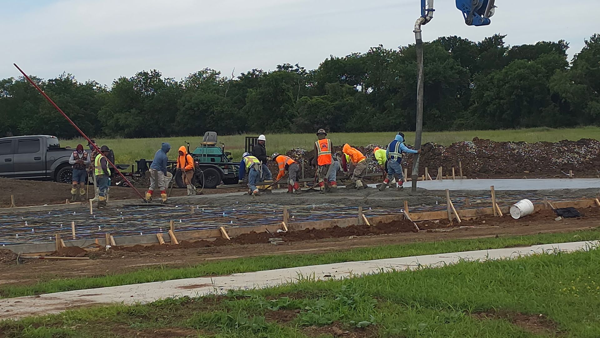 Workers in orange vests clear debris at a construction site with heavy equipment nearby.