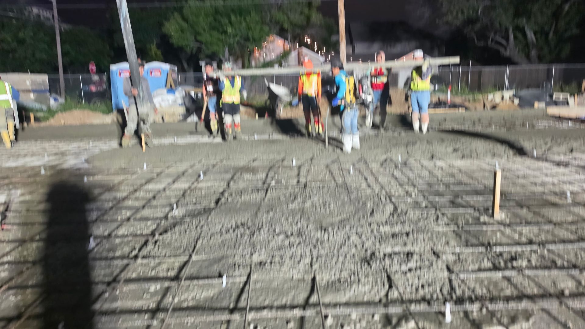 Construction crew leveling a rebar foundation at night, with workers and equipment in the background