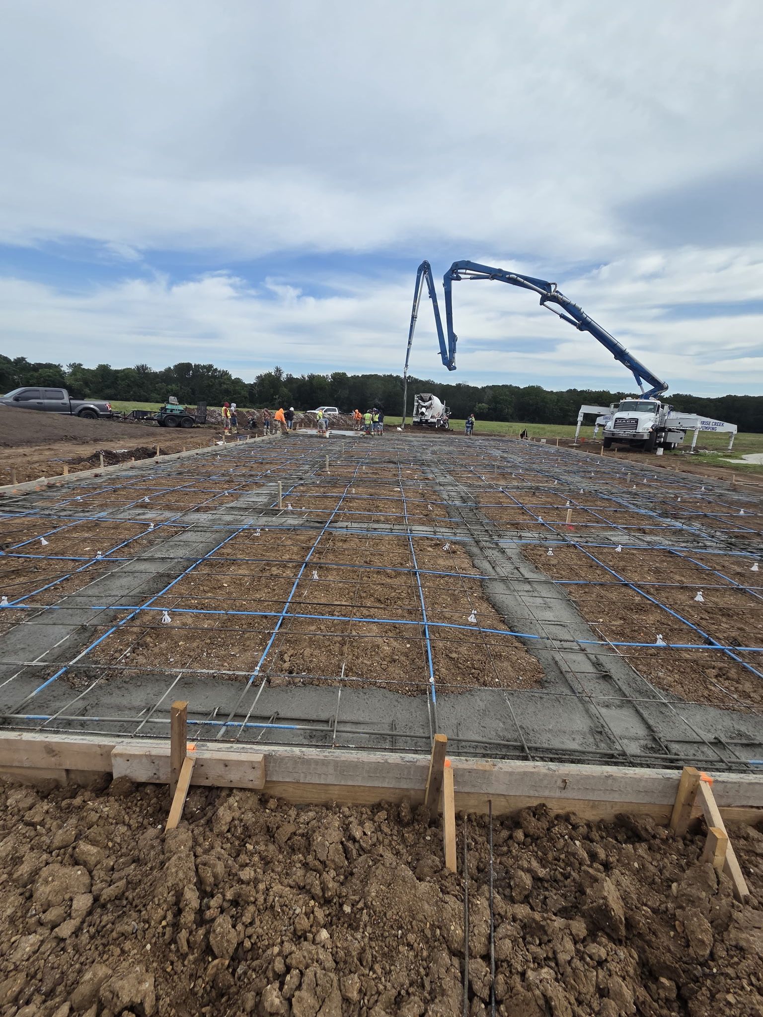 Construction site with concrete foundation, rebar grid, and a blue concrete pump truck in the distance