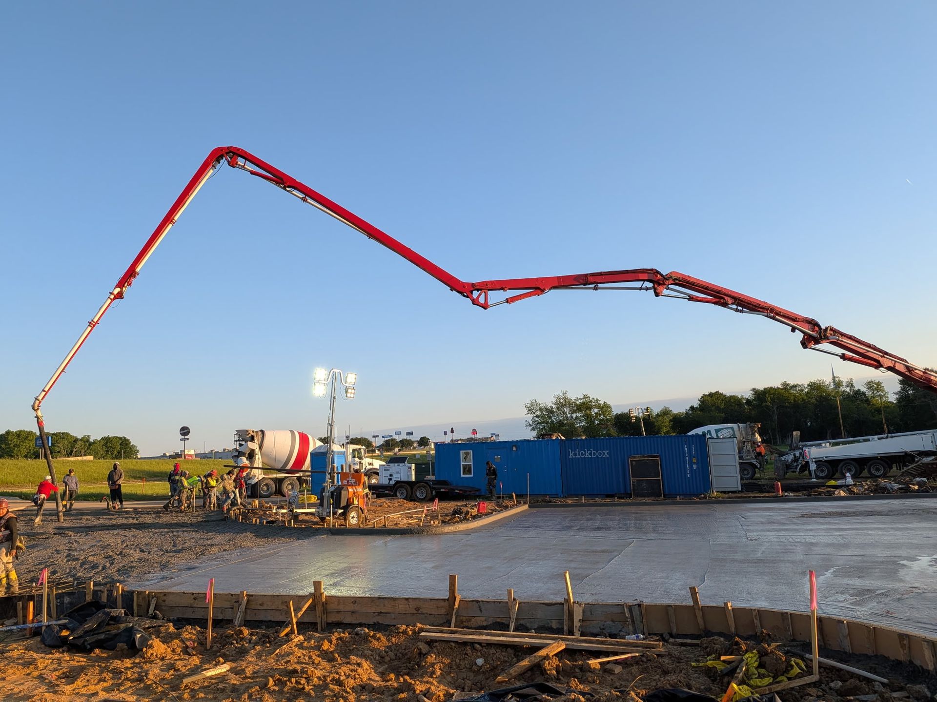 Concrete pump truck pouring at a construction site, with a long red boom over blue containers.