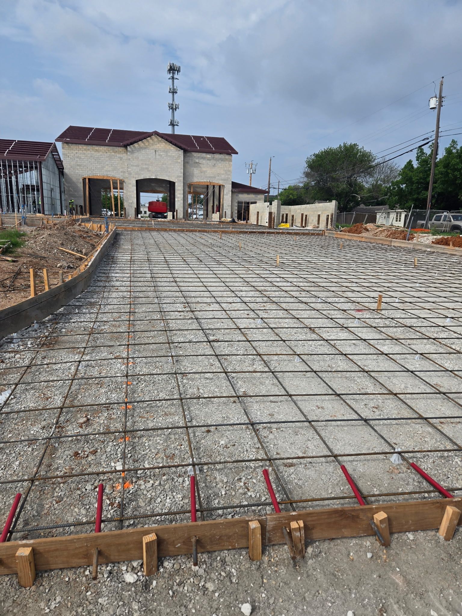 Construction site with rebar grid and concrete slab foundation in front of a partially built structure
