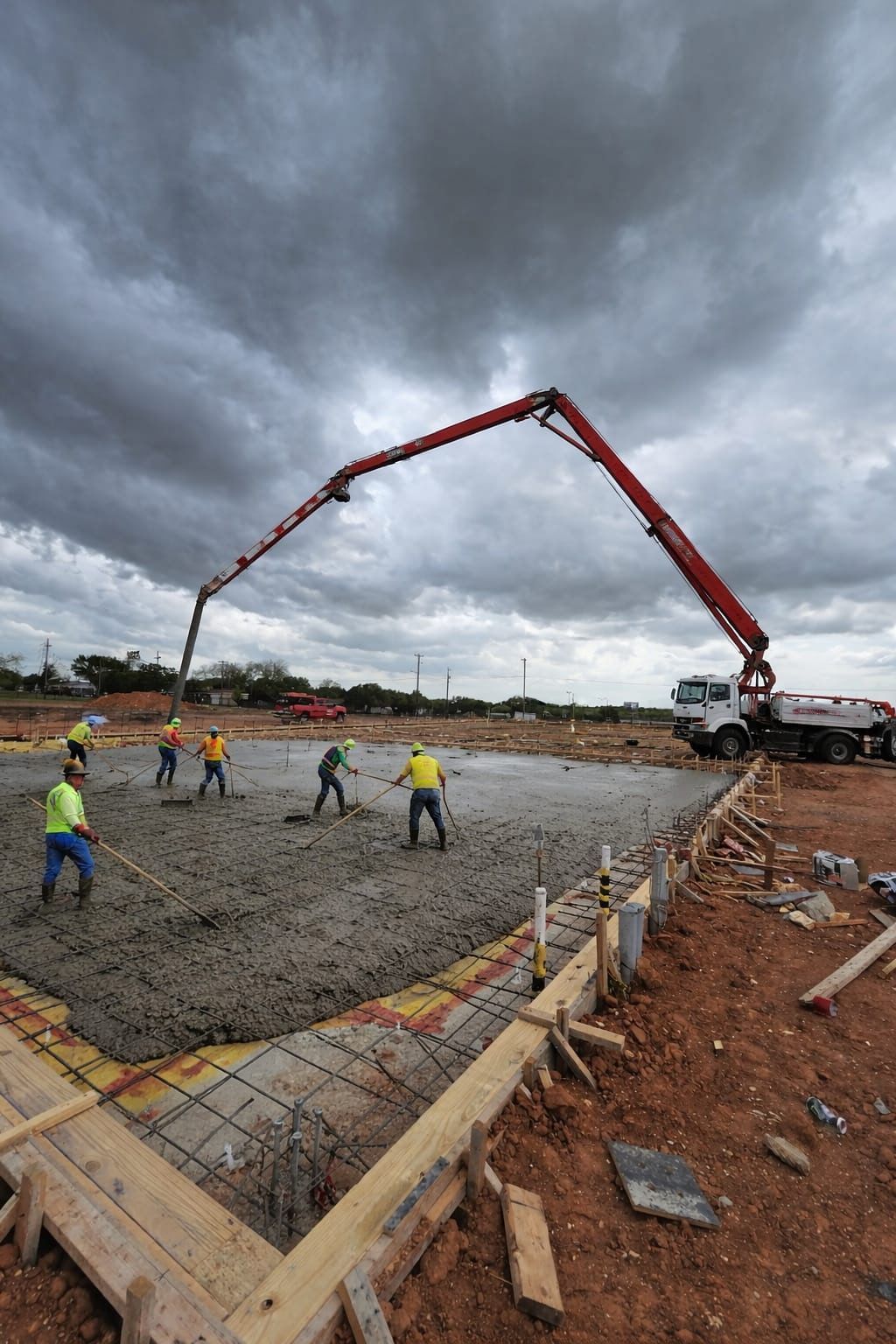 Workers pour concrete with a pump truck at a construction site under cloudy skies.
