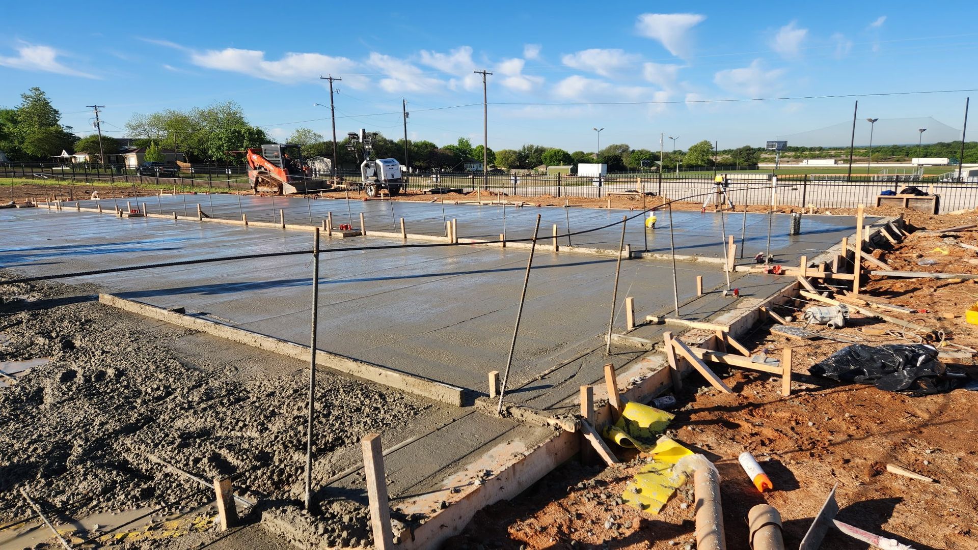 Construction site with concrete foundation forms, rebar, and wet slab under a blue sky