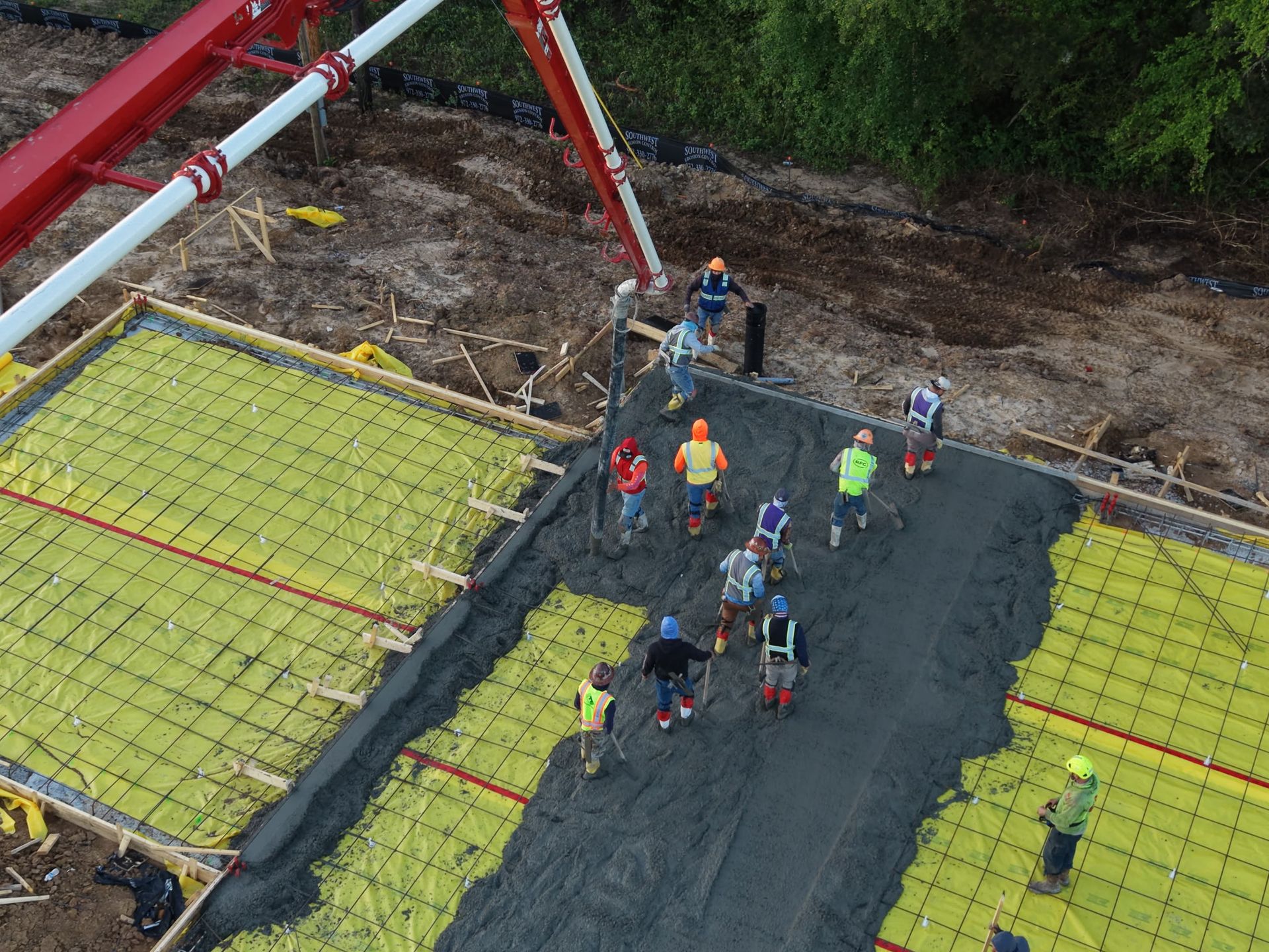 Workers placing concrete on a large foundation slab at a construction site.