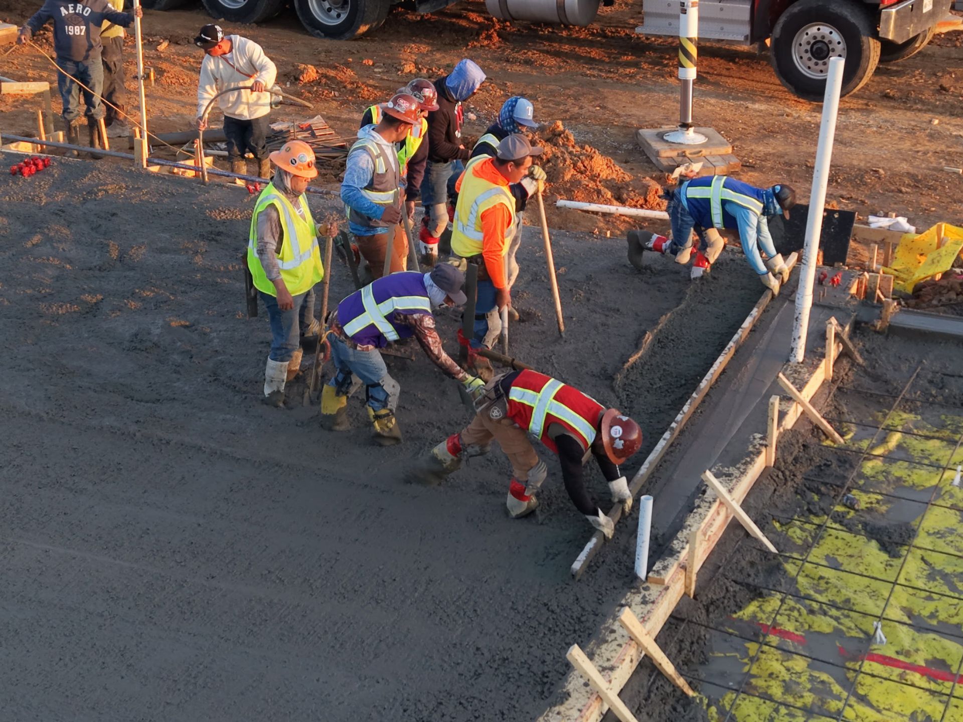 Construction crew paving a road, workers in safety vests and helmets smoothing fresh asphalt.