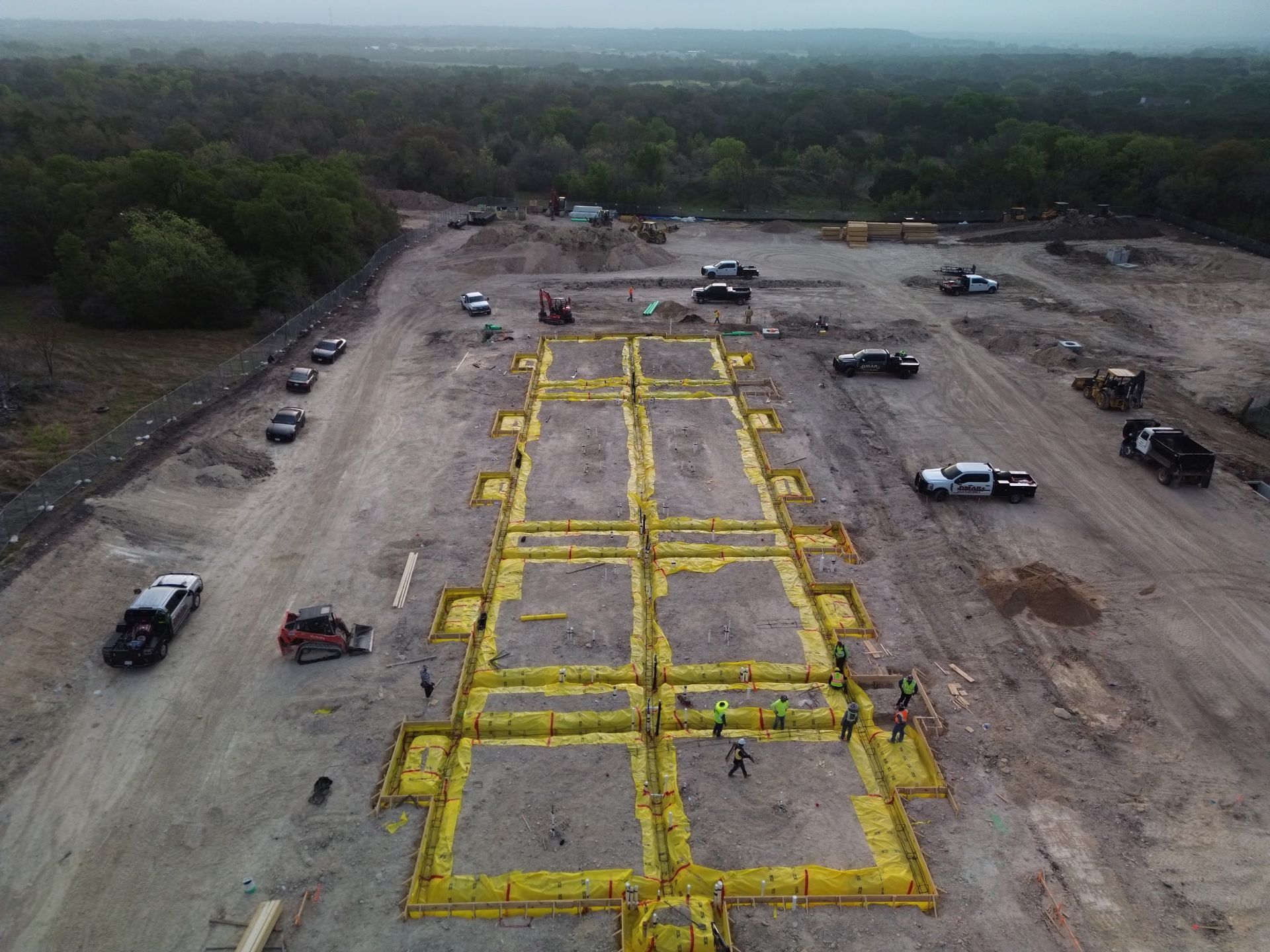 Aerial view of a dirt site with yellow grid-marked plots and several vehicles around the perimeter
