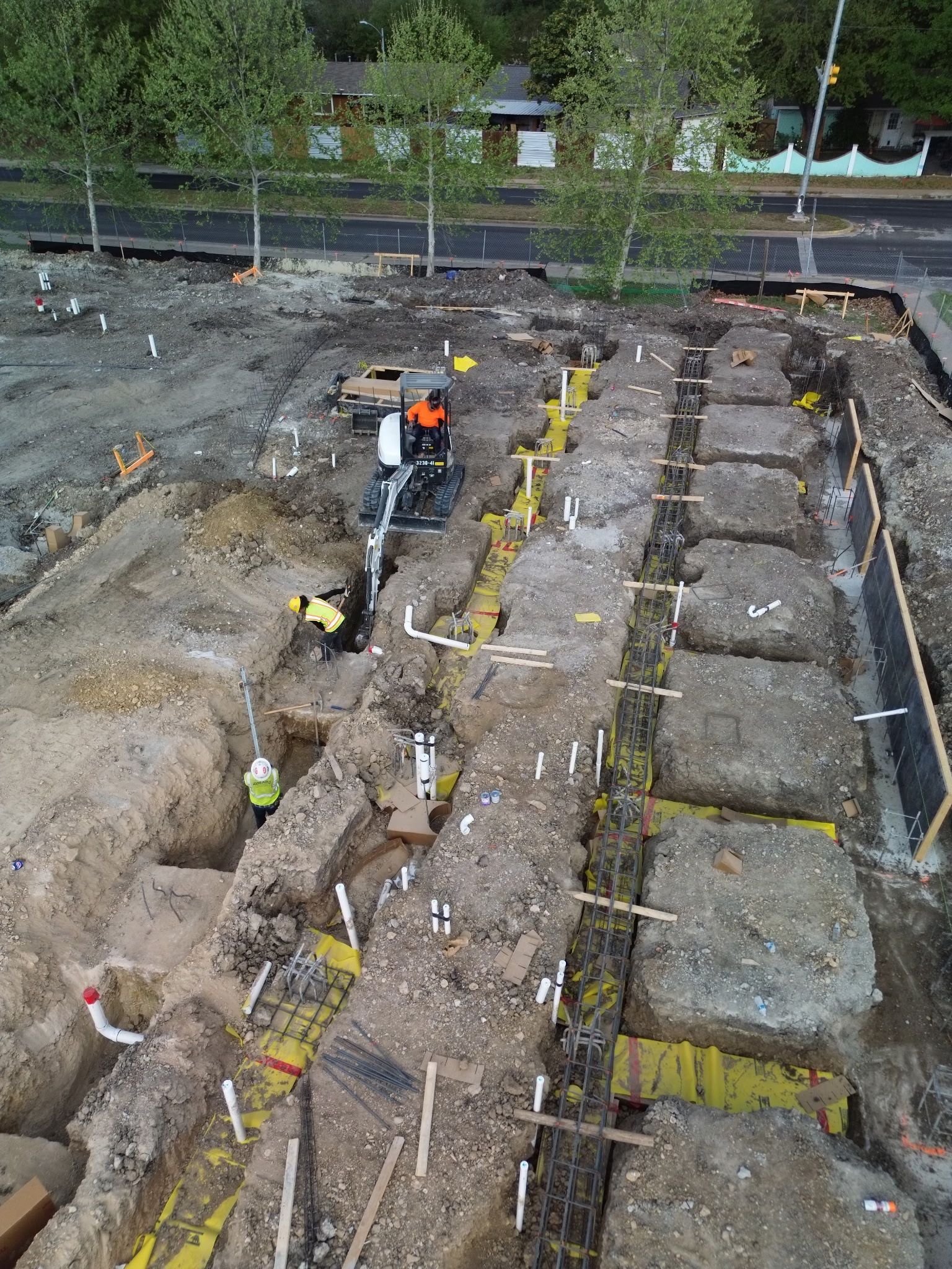 Archaeologists excavating a trench site with yellow markers and workers in orange vests