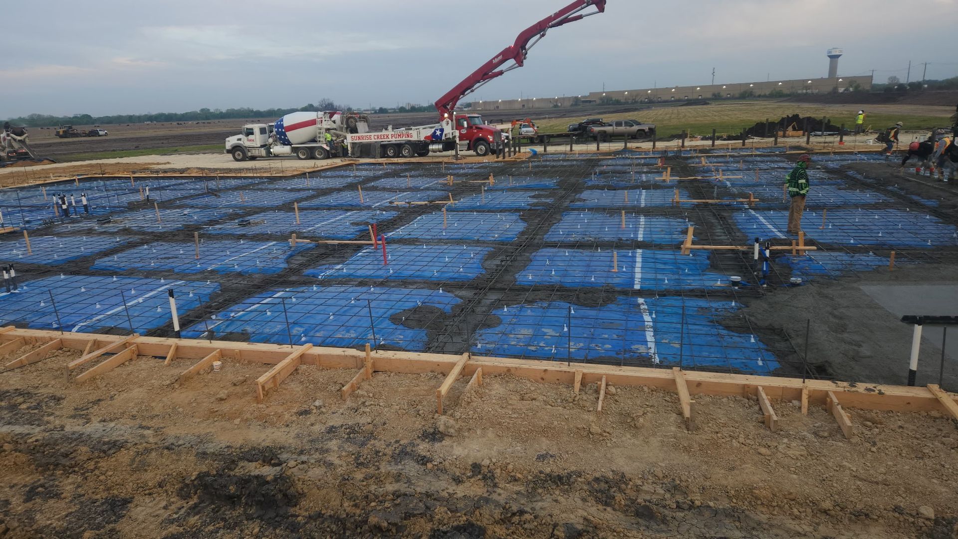 Construction site with blue-covered foundation and a concrete pump pouring on the right.