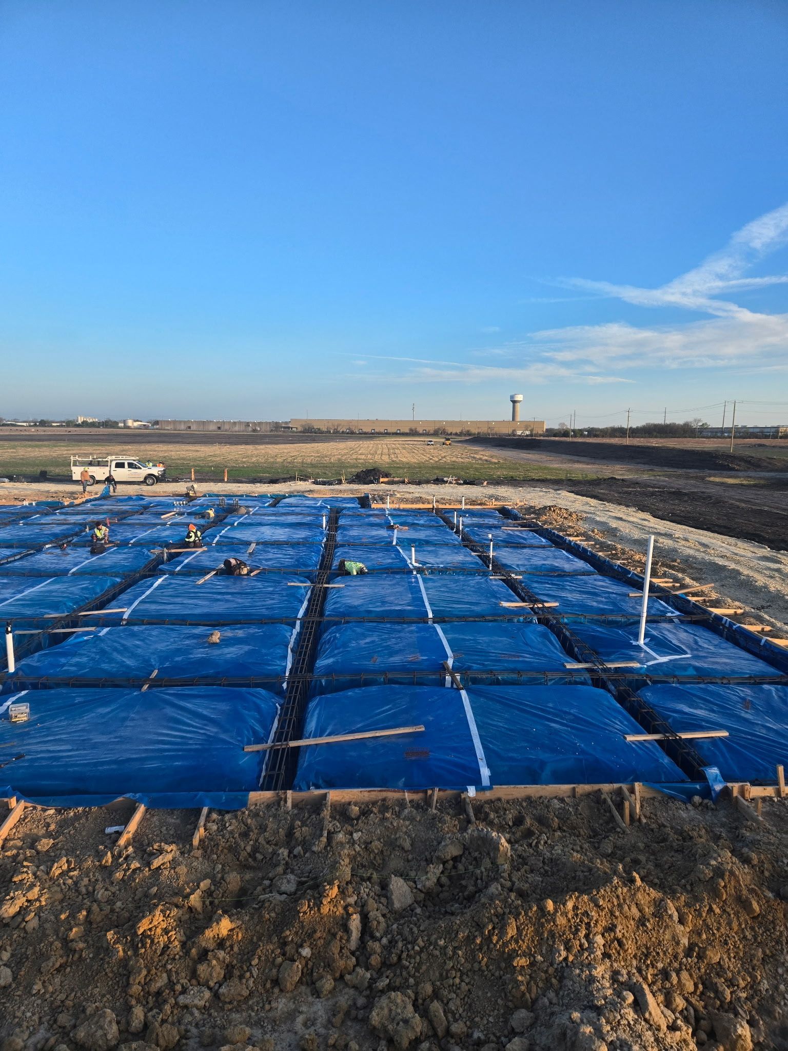 Blue-lined construction site with a large tarp-covered foundation in a barren landscape under a clear sky