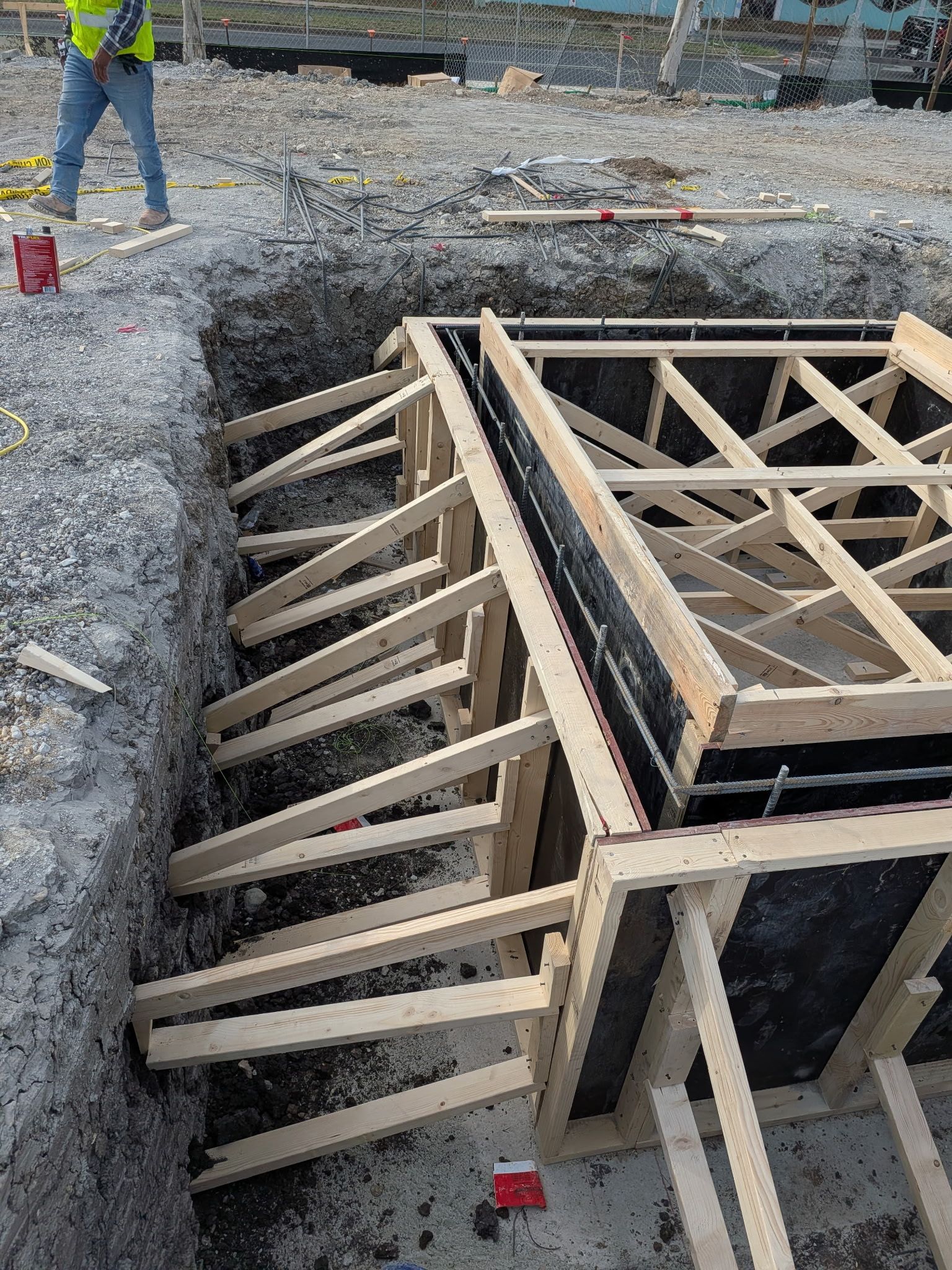 Construction site foundation formwork with wood framing and rebar, surrounded by gravel trench