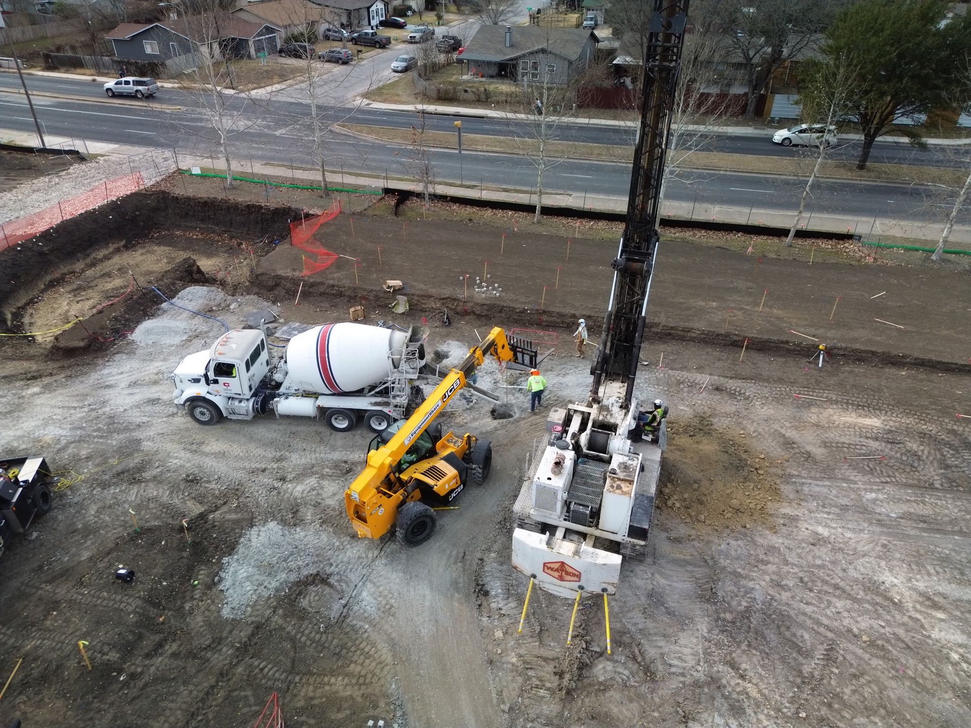 Construction crew with cement mixer and yellow excavator digging a trench beside a road