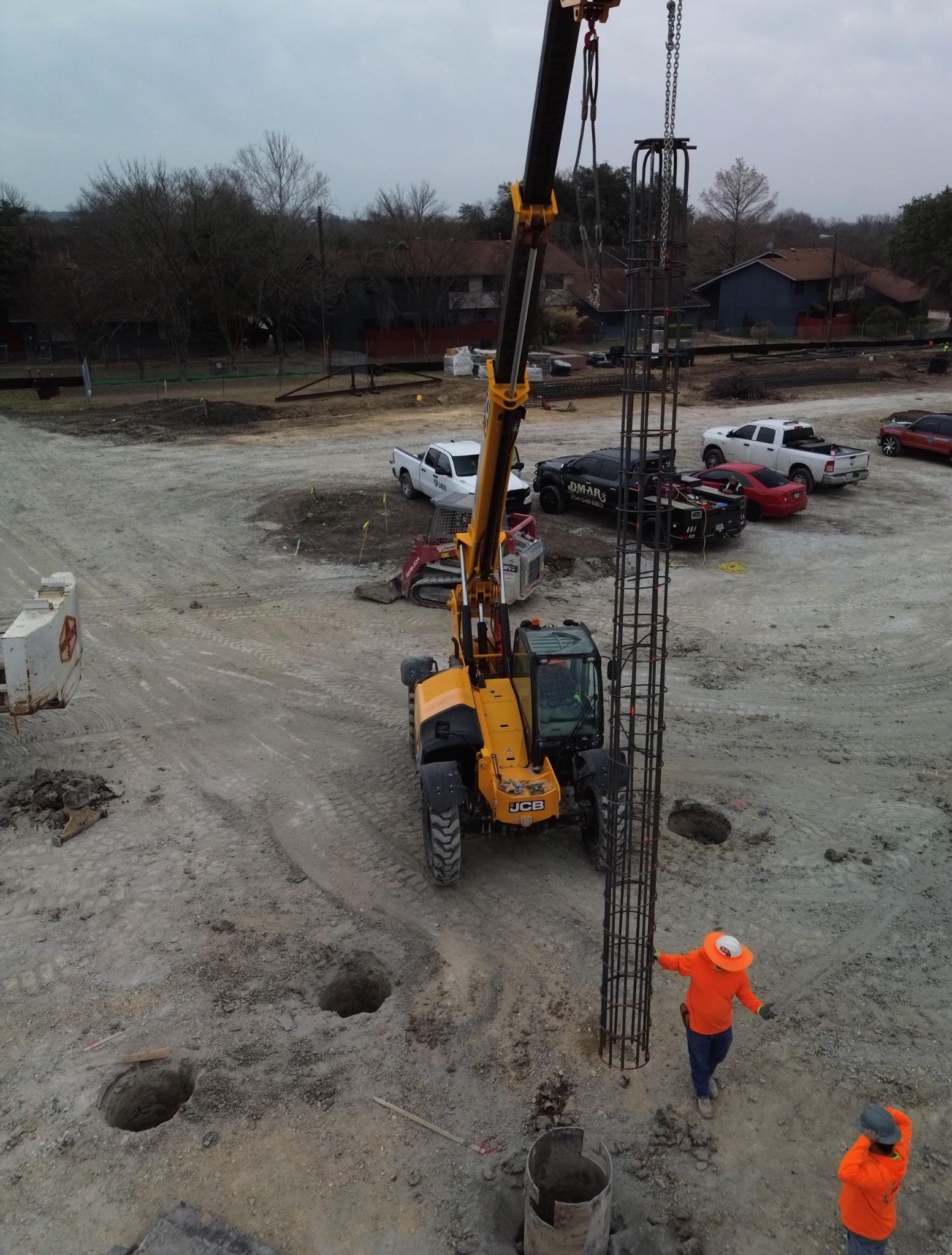 Construction site with yellow drilling rig and two workers in orange safety gear beside deep holes