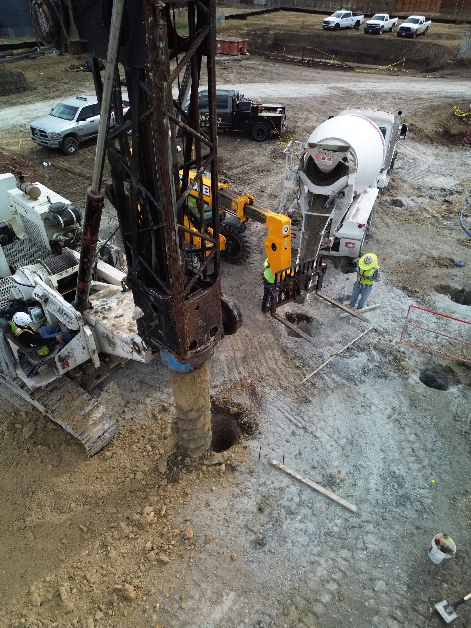 Construction site with drilling rig, cement mixer truck, and workers on gravel ground