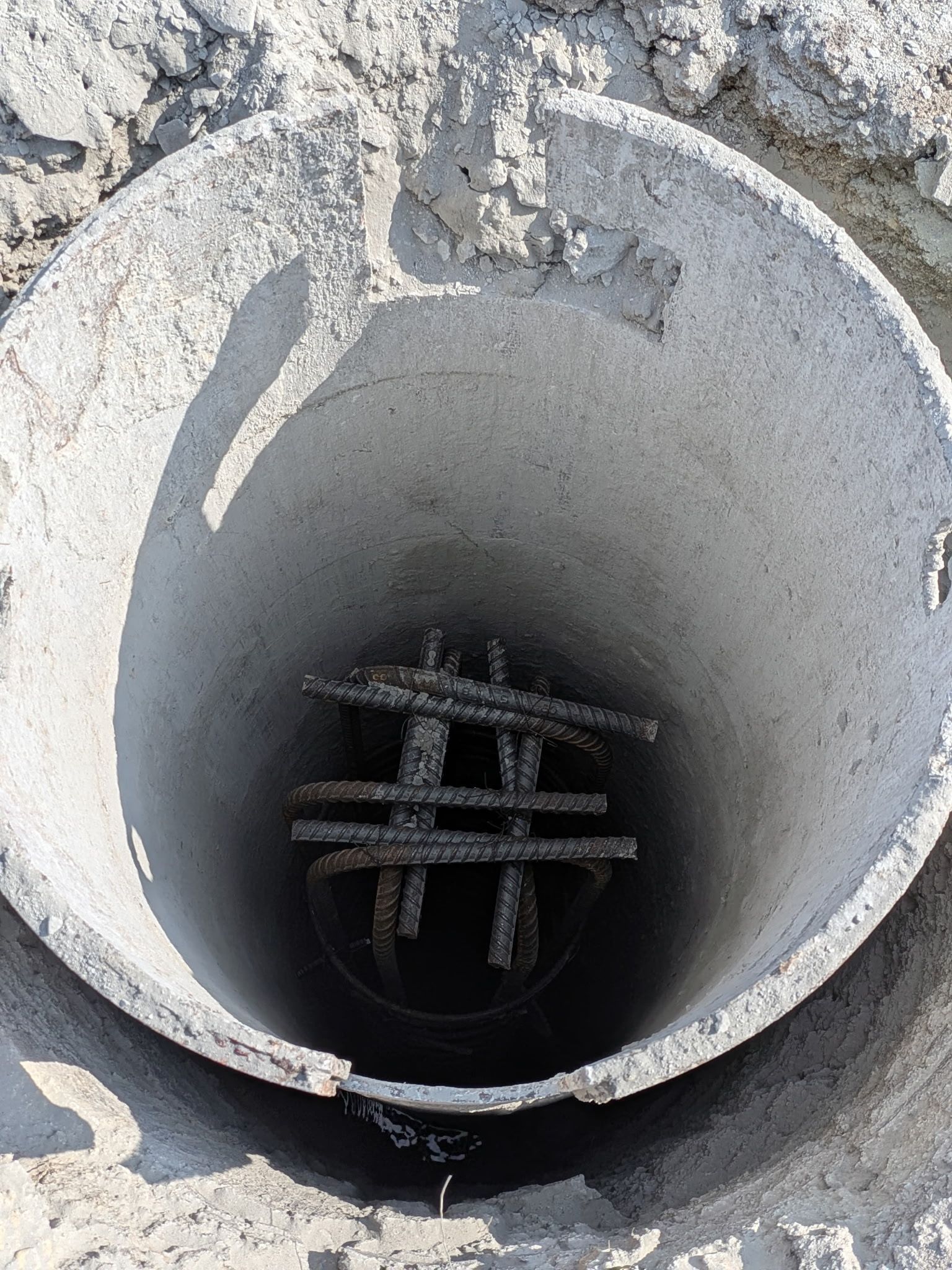 Concrete manhole with rebar visible inside an open circular shaft