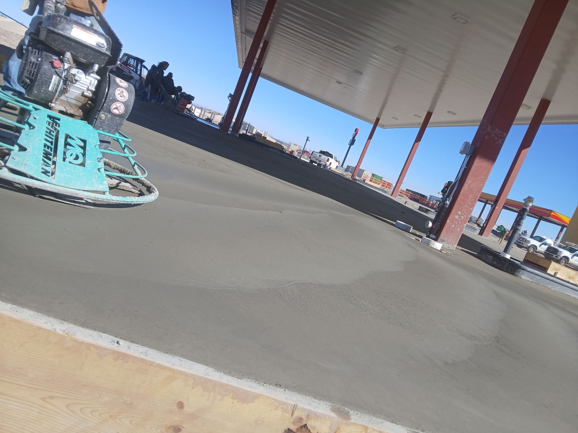 Blue race car parked under a gas station canopy on a sunny day, with another car in the background.