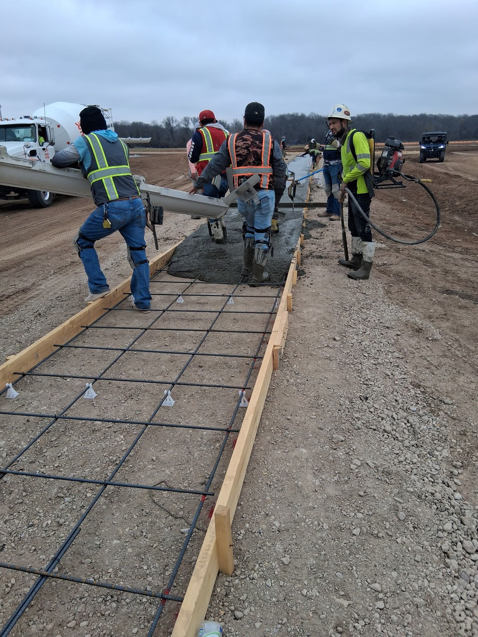 Construction workers pouring concrete into a wooden form for a walkway at an outdoor site.