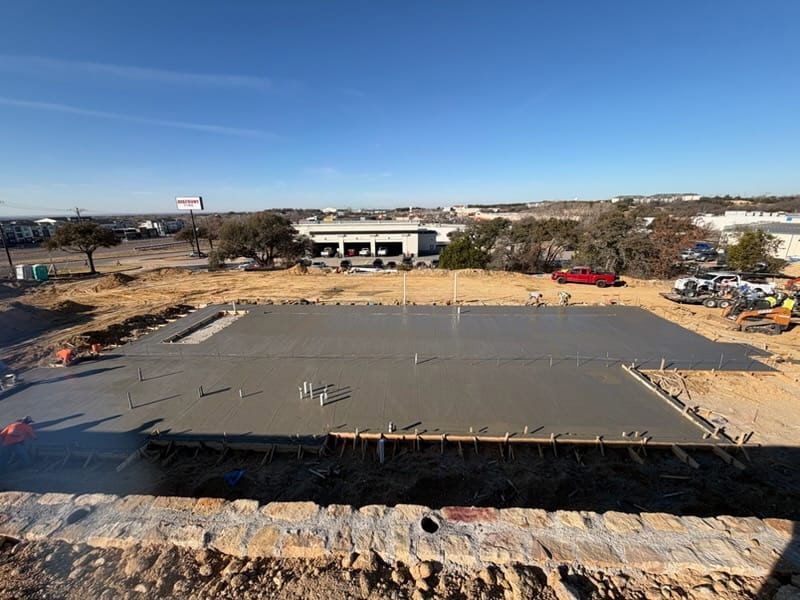 Construction site with a large concrete foundation slab and workers in the distance under a clear blue sky