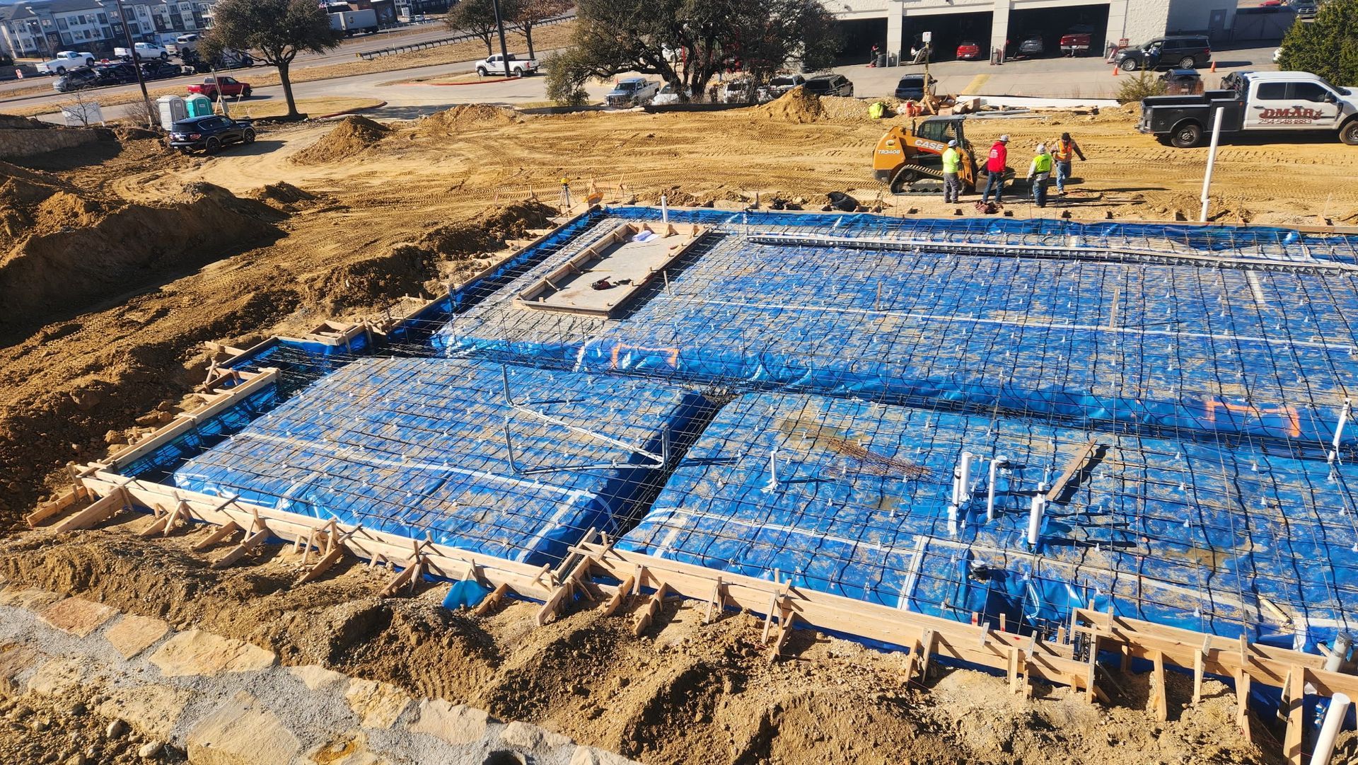 Construction site with blue tarp-covered foundation and workers in the background