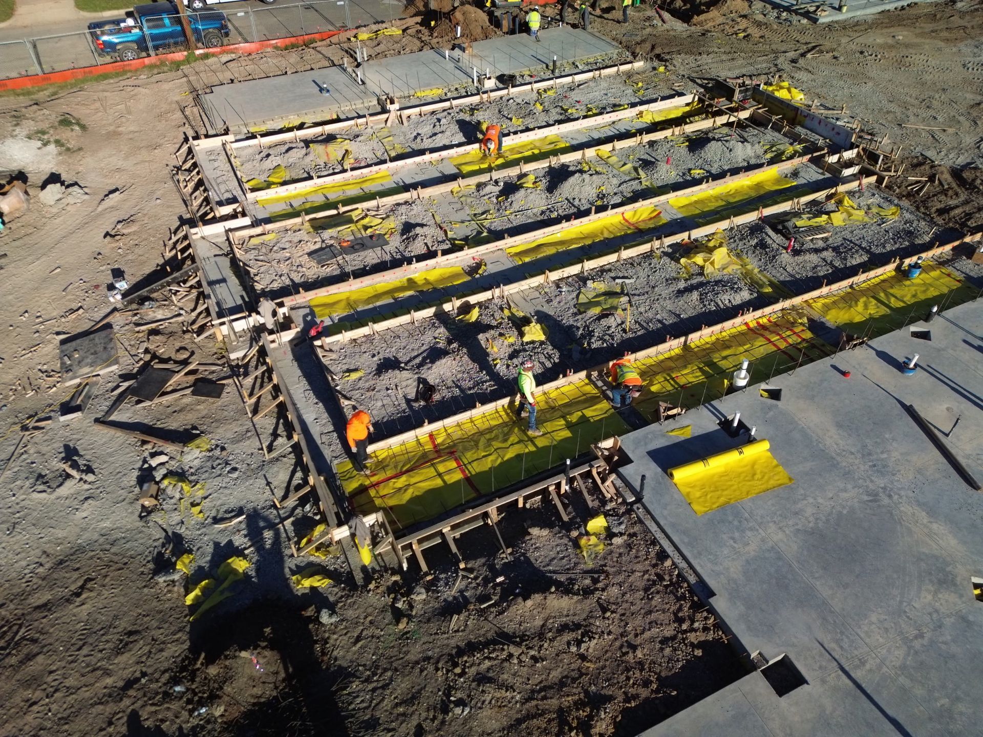 Construction site with workers installing yellow beams in a concrete foundation pit