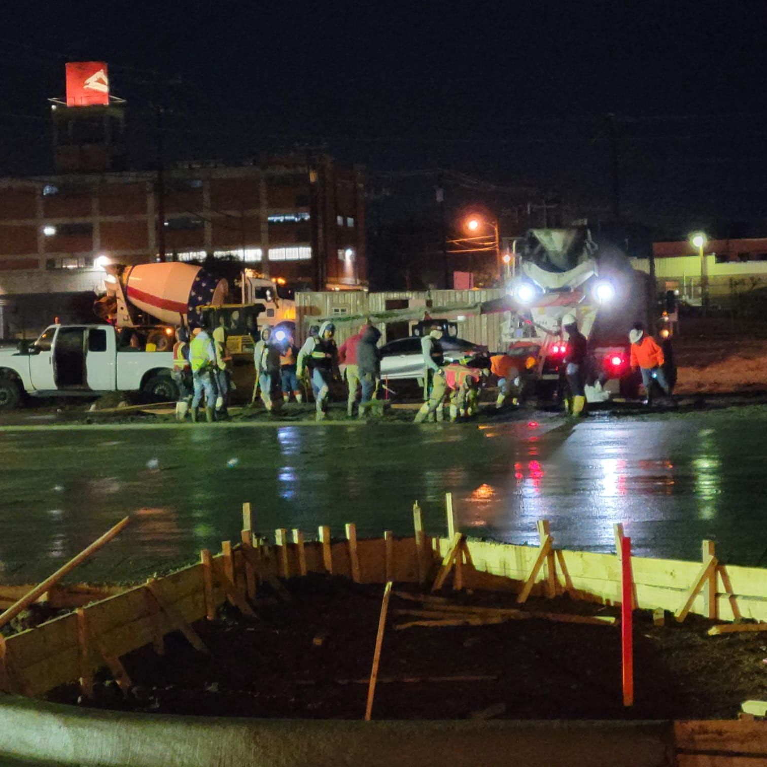Workers and trucks at a nighttime construction site around a wet concrete pour