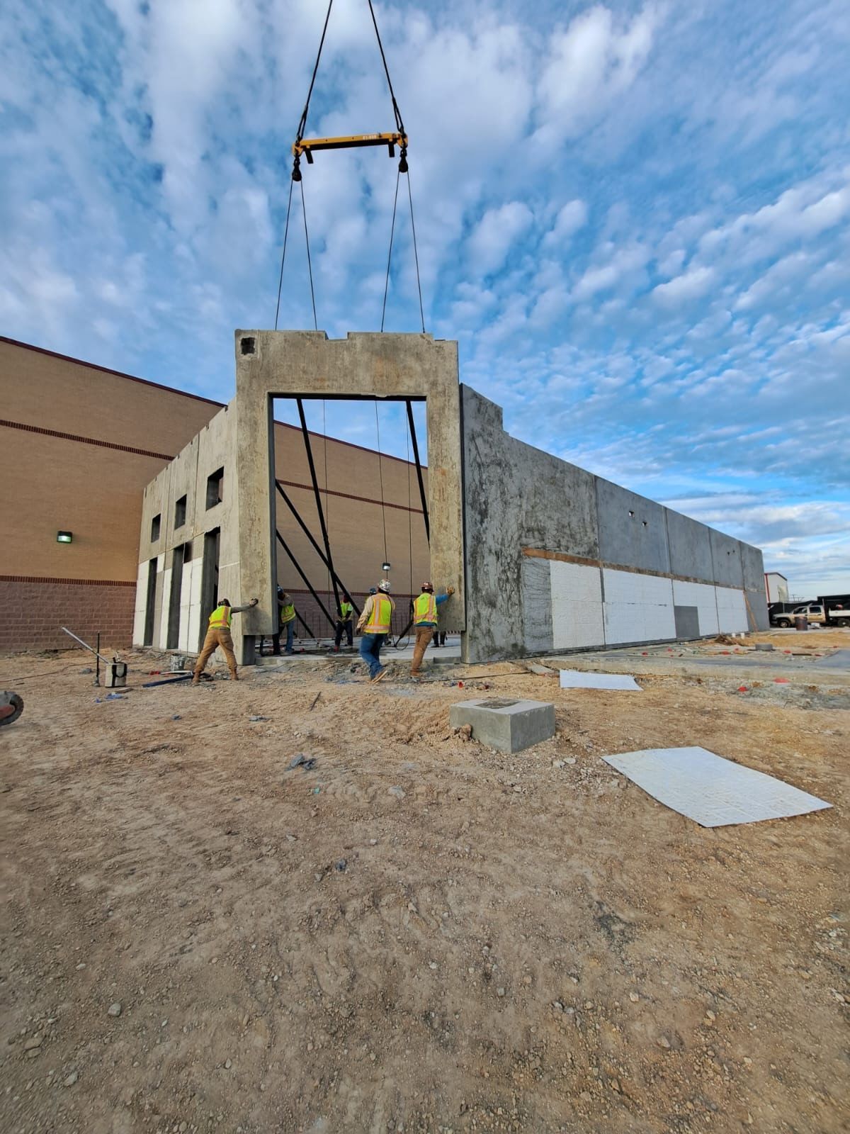 Construction workers installing a concrete wall panel at a building site with a crane.