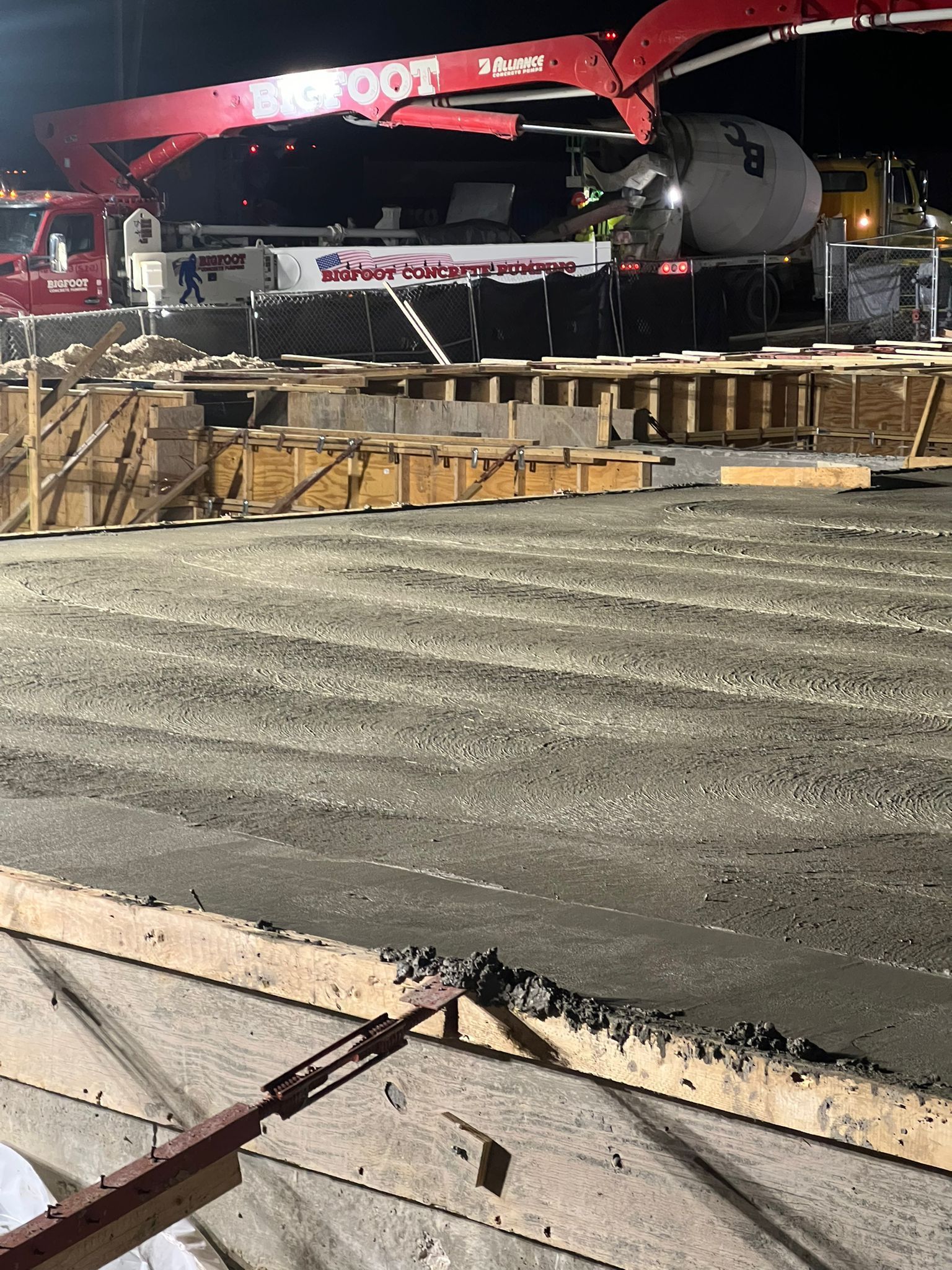 A concrete pump is pouring concrete on a construction site at night.