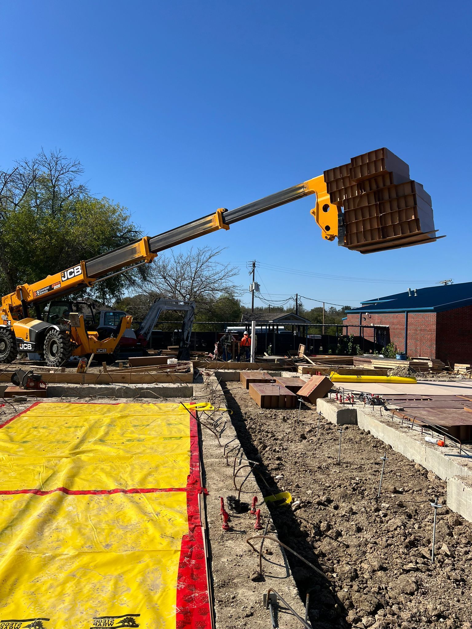 A crane is lifting a pallet of bricks on a construction site.