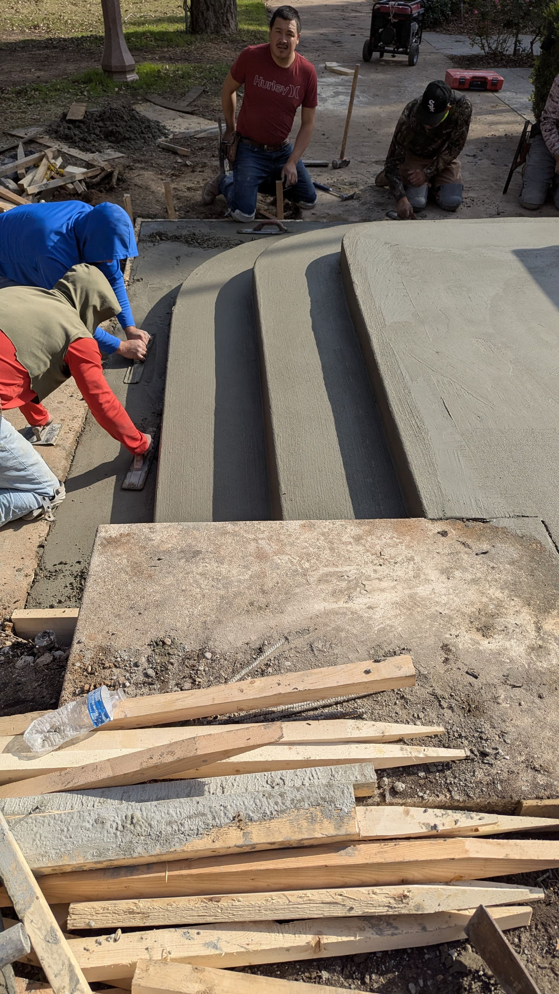A group of construction workers are working on a concrete driveway.