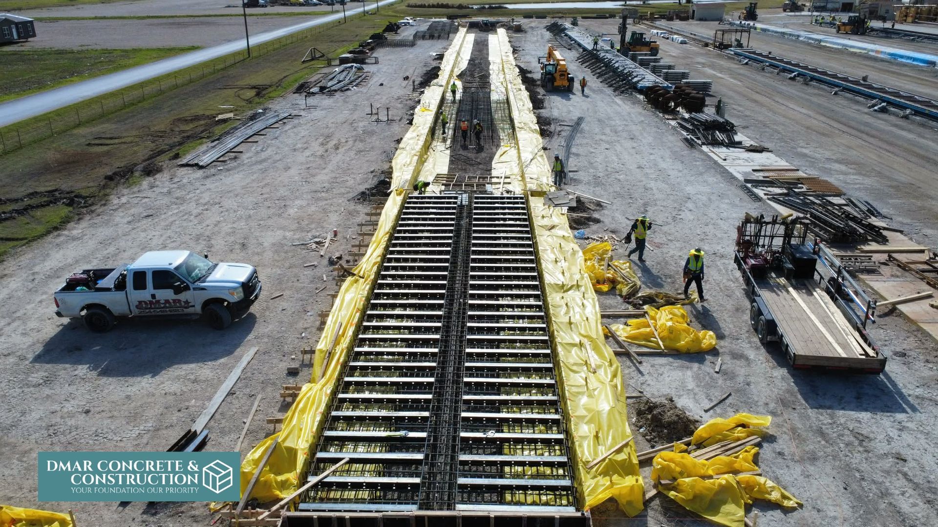 Construction site with railroad tracks under repair, yellow materials along the rails, and work trucks nearby.