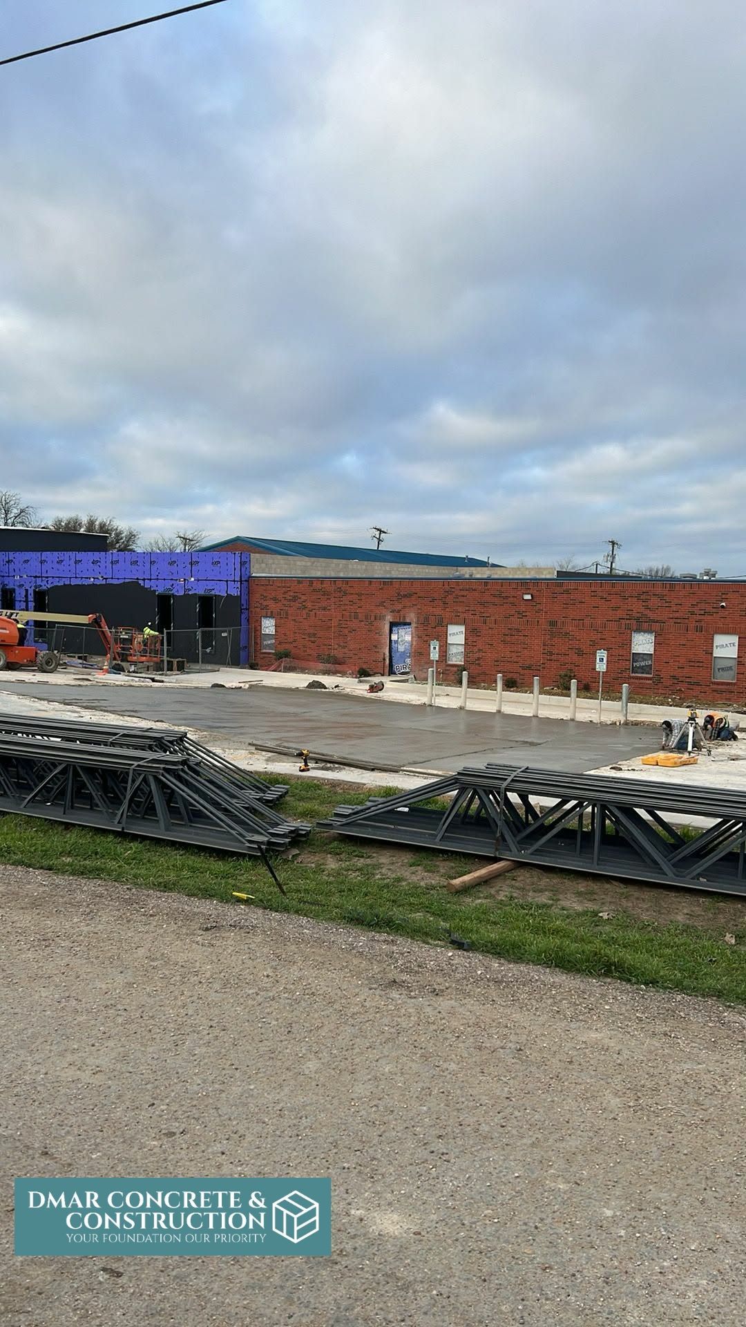 Construction site with brick building, gravel foreground, metal beams, and cloudy sky