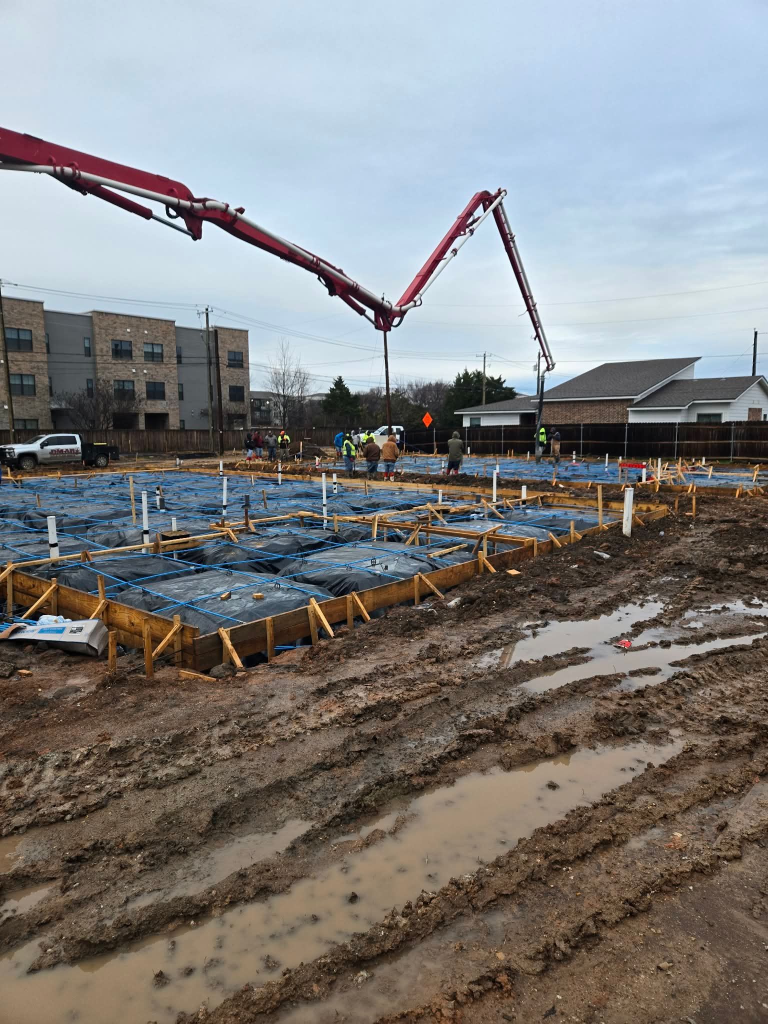 Construction site with concrete pump boom over rebar foundation on a muddy, overcast day