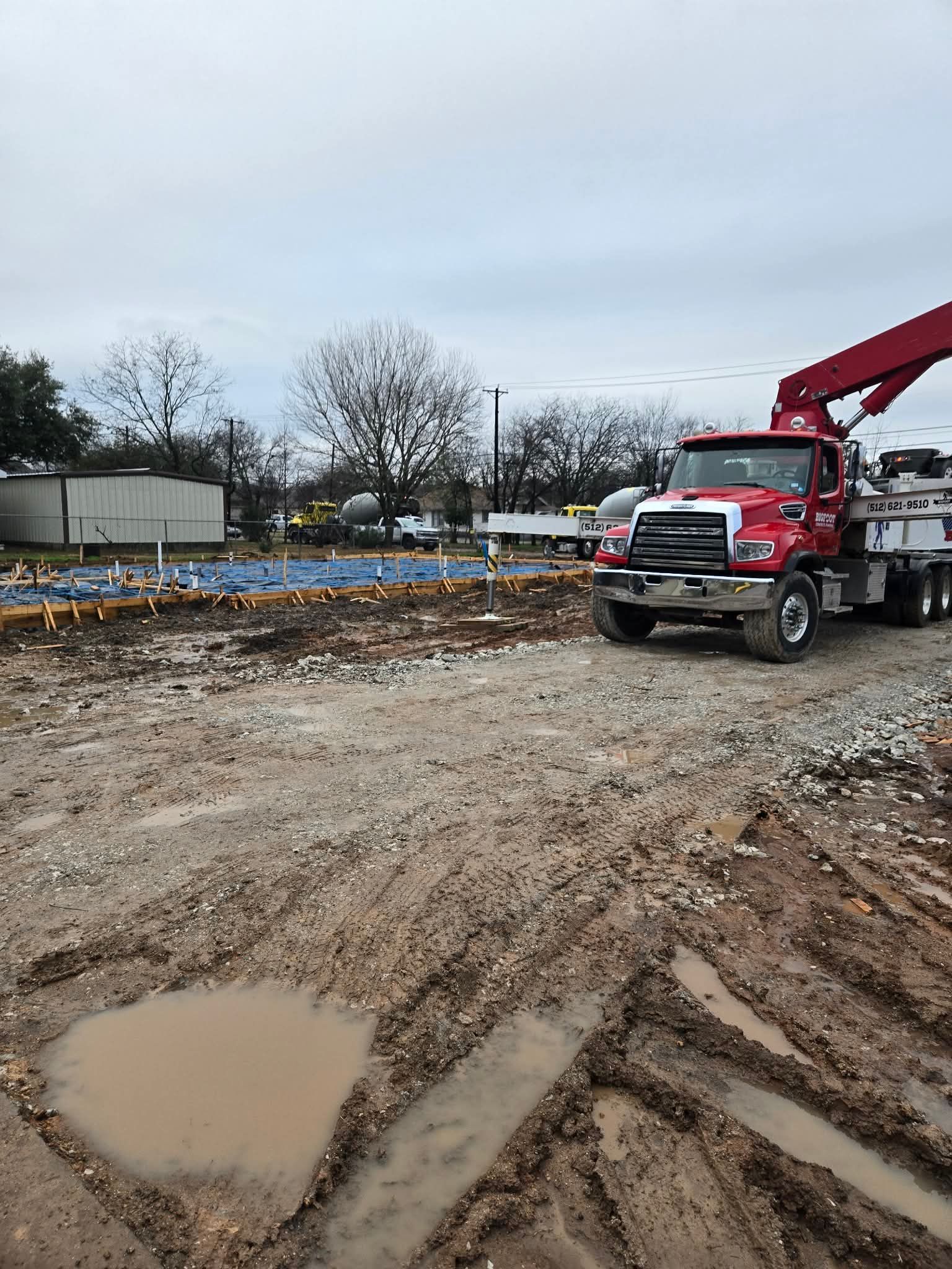 Red tow truck at a muddy construction site with a puddle in the foreground