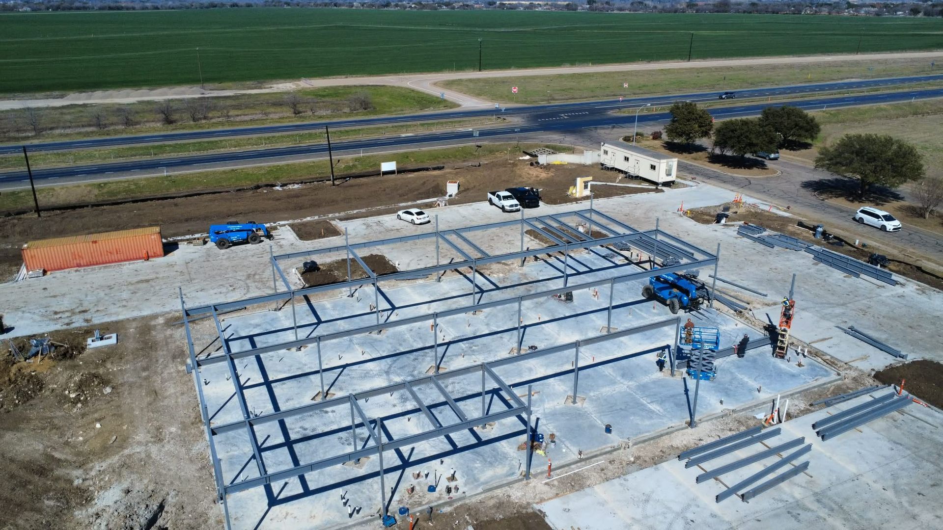 Steel frame building under construction on a concrete foundation in a rural field.