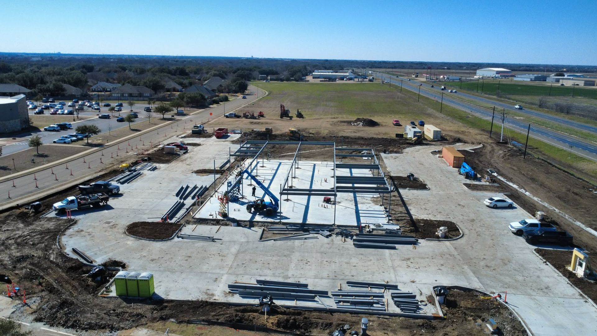 Aerial view of a large construction site with a concrete foundation, materials, and open land around it.