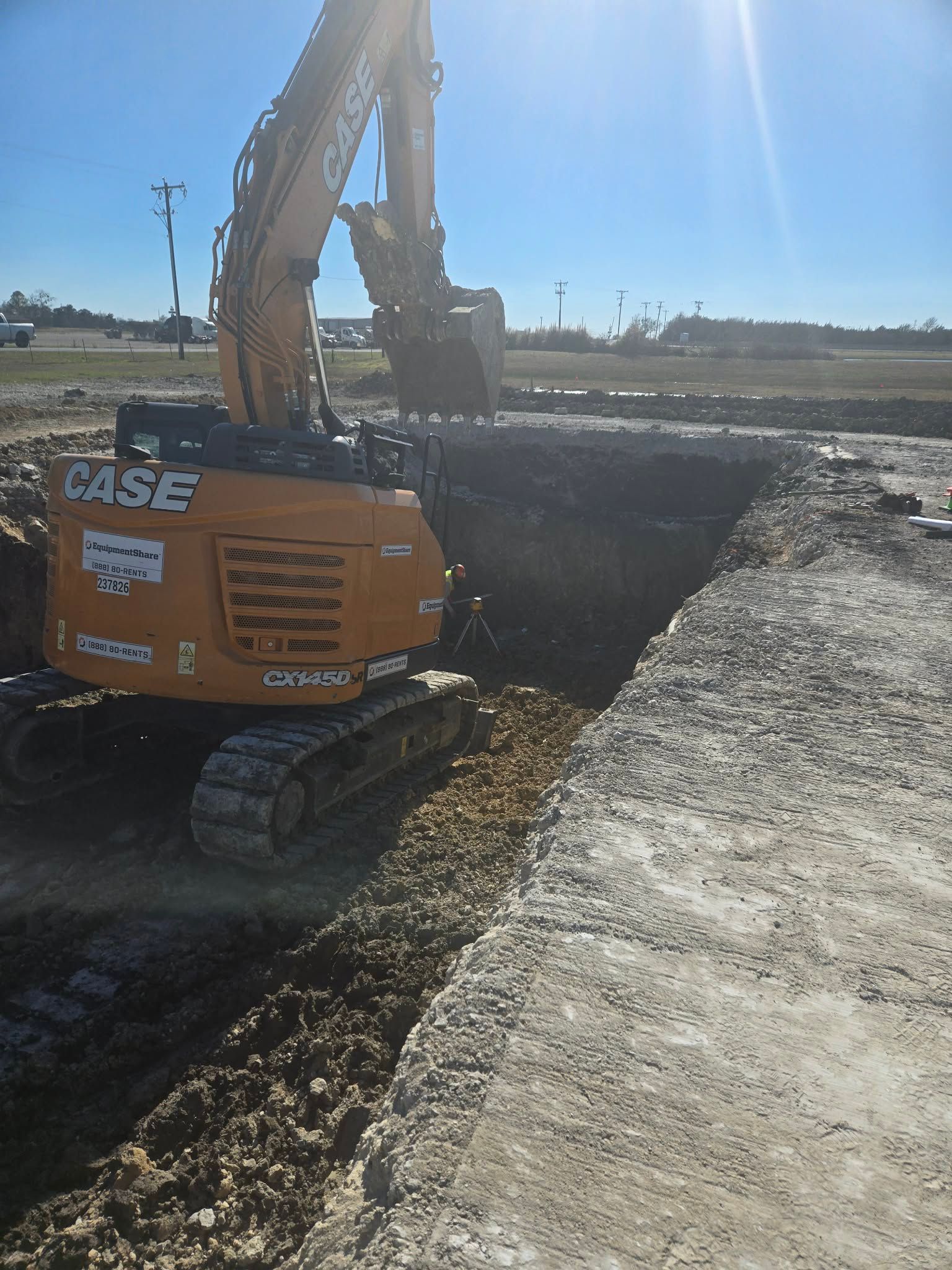 Orange CASE excavator working beside a muddy trench on a sunny construction site