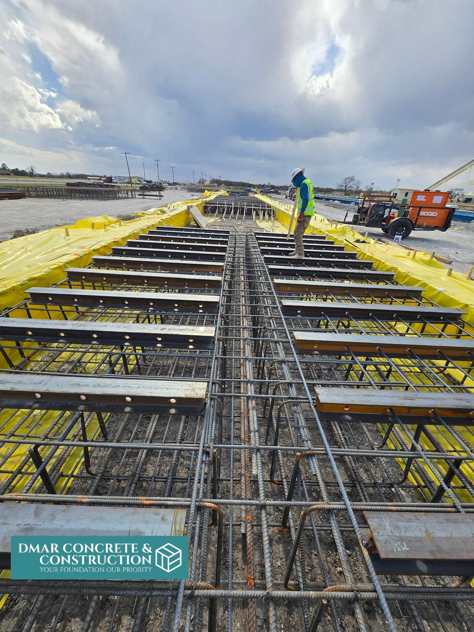 Construction site with steel rebar deck, yellow formwork, and workers under a cloudy sky