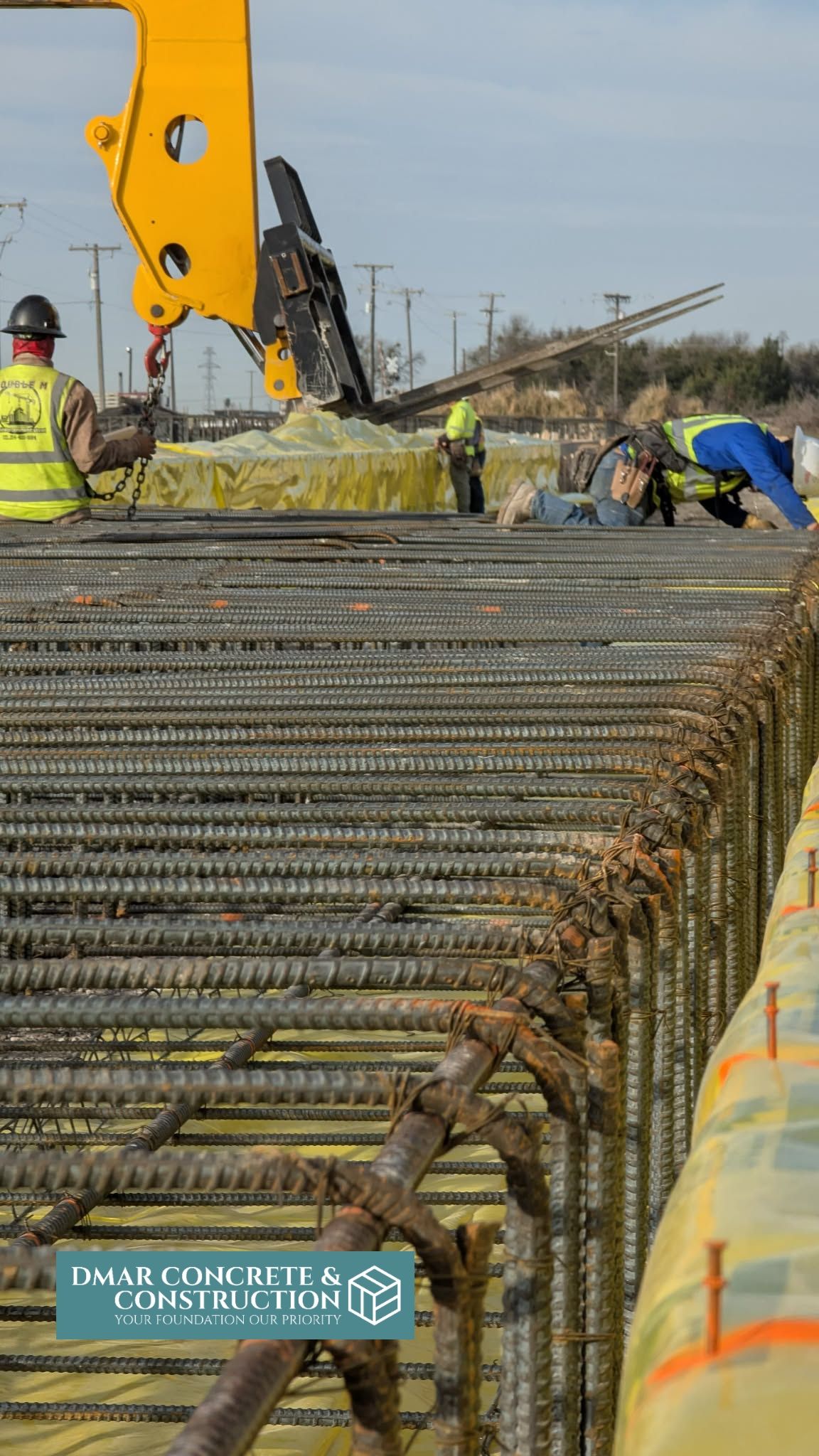 Workers beside a yellow excavator on a steel rebar foundation at a construction site