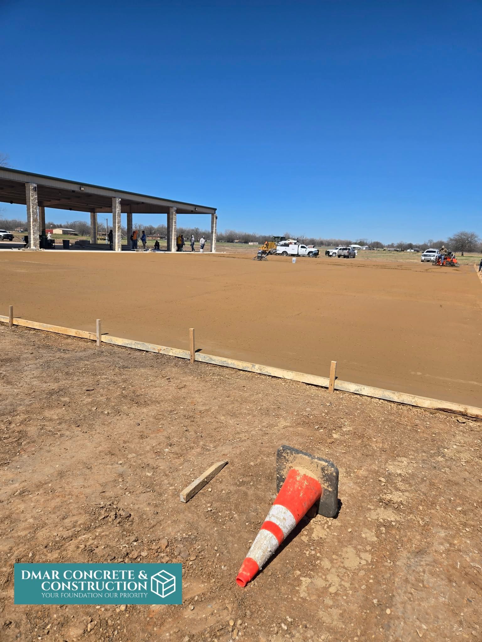 Orange traffic cone on sandy lot near a covered structure under a clear blue sky.