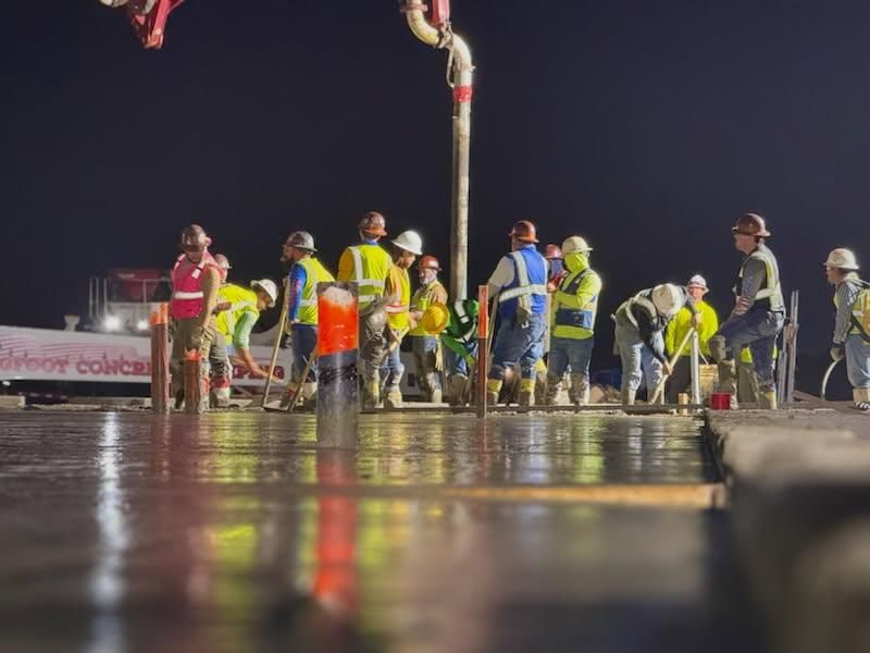 A group of construction workers are standing around a pole at night