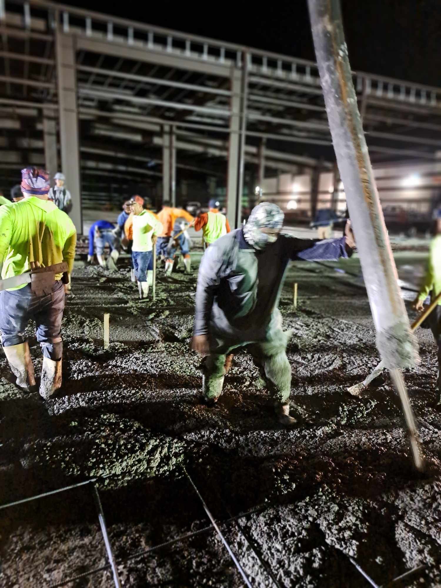A group of construction workers are working on a concrete floor at night.