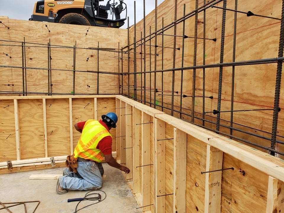 A construction worker is kneeling down in front of a wooden wall.
