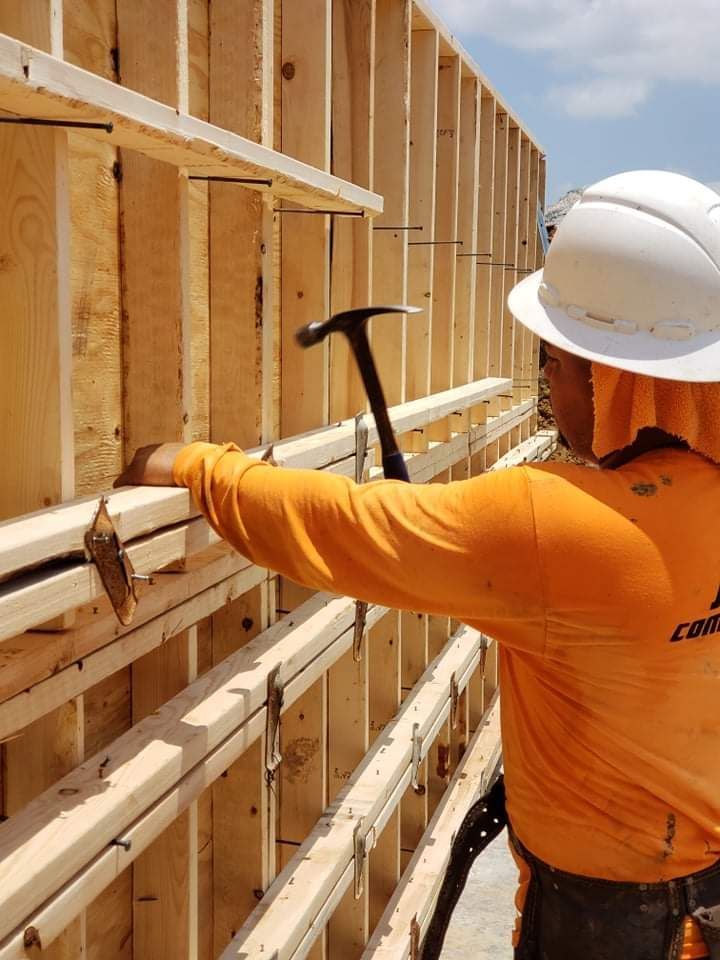 A man wearing a hard hat and an orange shirt is working on a wooden wall