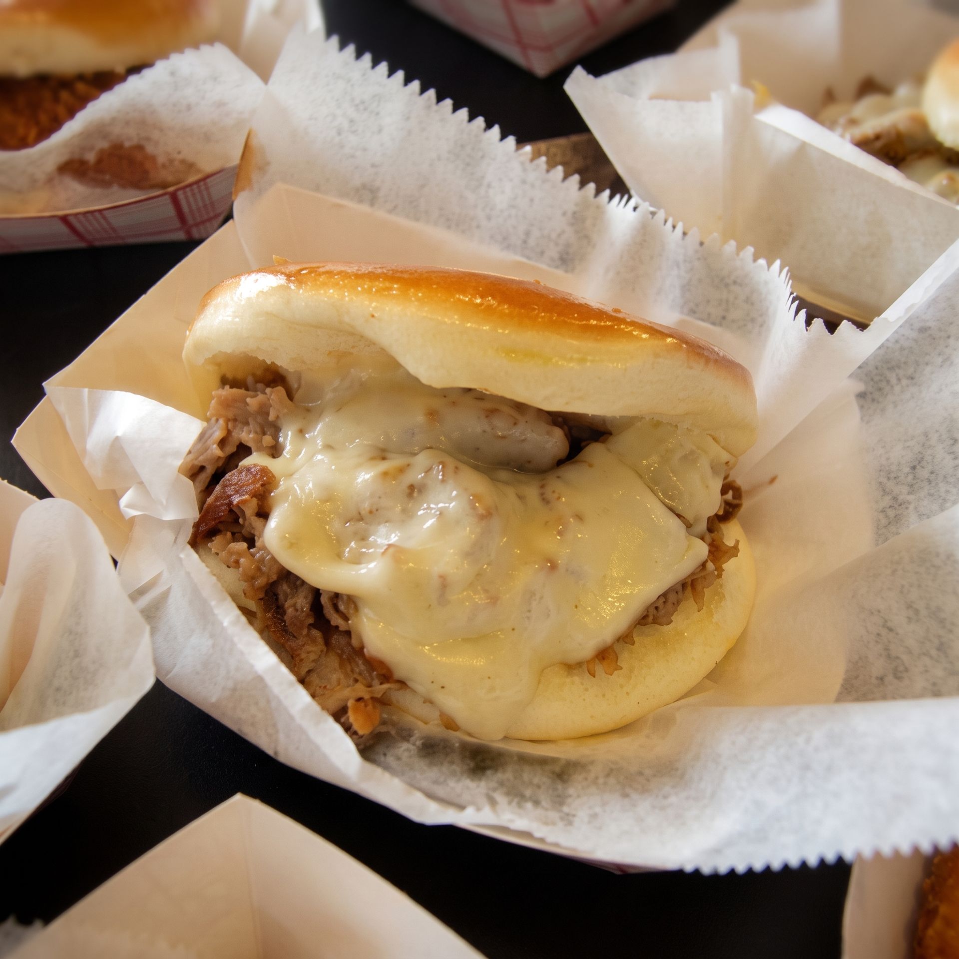 Cheeseburger with melted cheese in a paper wrapper, on a tray with other wrapped sandwiches nearby