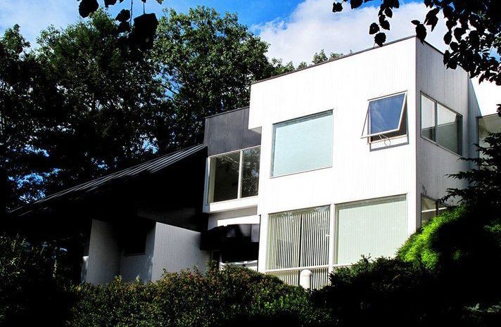 A white house with a black roof is surrounded by trees