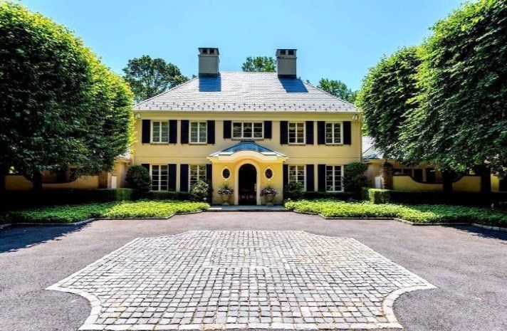 A large yellow house with a brick driveway in front of it